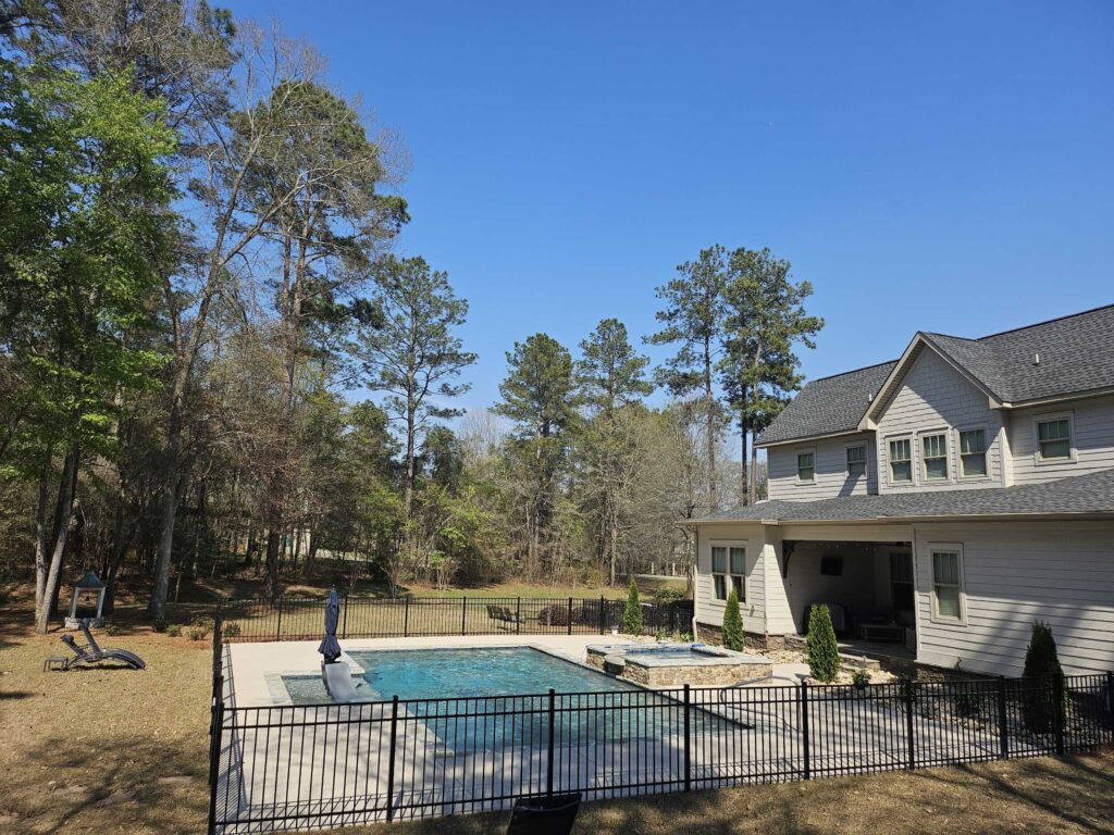 Aerial view of a fenced inground pool with attached hot tub and lounge chairs beside a two-story home in Warner Robins Georgia