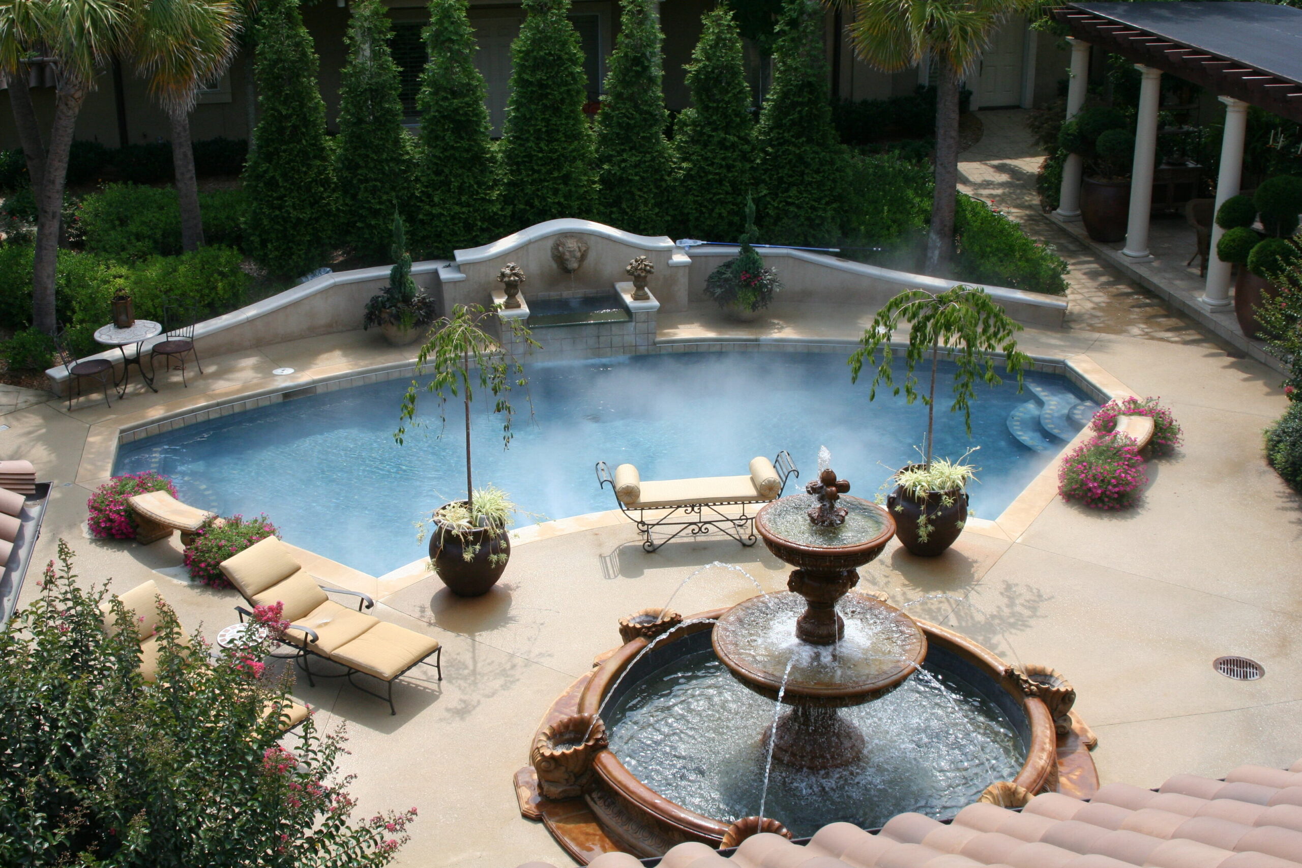 Aerial view of custom gunite pool with integrated spa, stone coping, lounge chairs and umbrellas in private wooded backyard